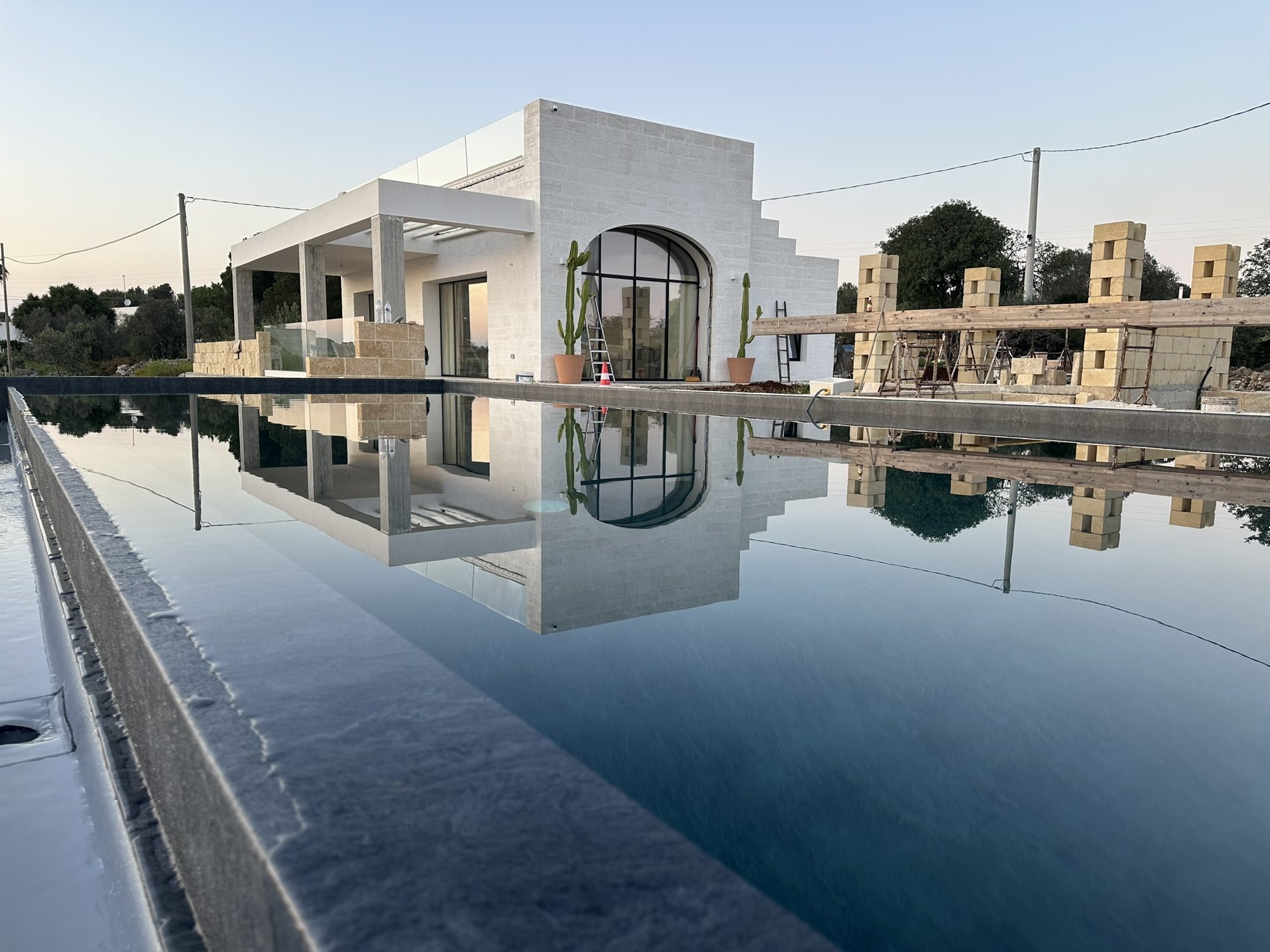 Villa en pierre blanche reflétée dans la piscine à débordement